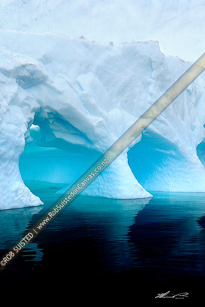 Photo of Iceberg with water sculptured hollows and caves, in calm dark water. Irridescent luminious blues, Antarctic Peninsula, Antarctica, Antarctica Region, Antarctica