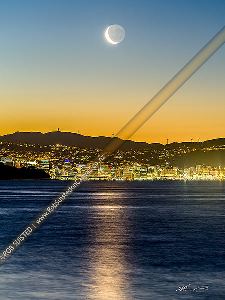 Photo of Wellington City CBD twilight with setting moon at sunset, seen from eastern harbour. Waning crescent moon phase. Large telephoto lens image, Wellington, Hutt City, Wellington Region, New Zealand (NZ)